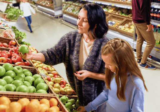 Женщина помогает мужчине в инвалидном кресле достать продукт с нижней полки в магазине